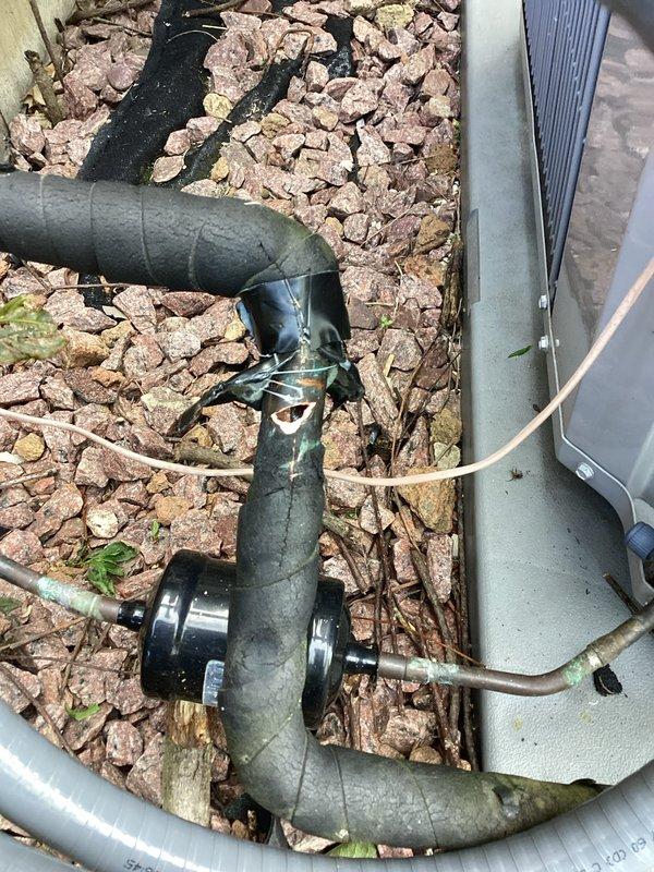Responded to no cooling complaint on residential air conditioning system. Upon arrival, discovered refrigerant line set had been physically damaged during recent landscaping activities, resulting in complete refrigerant loss from the system. Inspected outdoor condensing unit and traced refrigerant lines to identify extent of damage. Found compromised section of line set where landscape work had impacted the copper tubing, causing puncture and subsequent leak. Documented equipment information and damage with photographs showing affected refrigerant lines, insulation, and outdoor unit positioning. System was rendered inoperable due to complete loss of refrigerant charge from damaged line set requiring repair or replacement of affected section and system recharge.