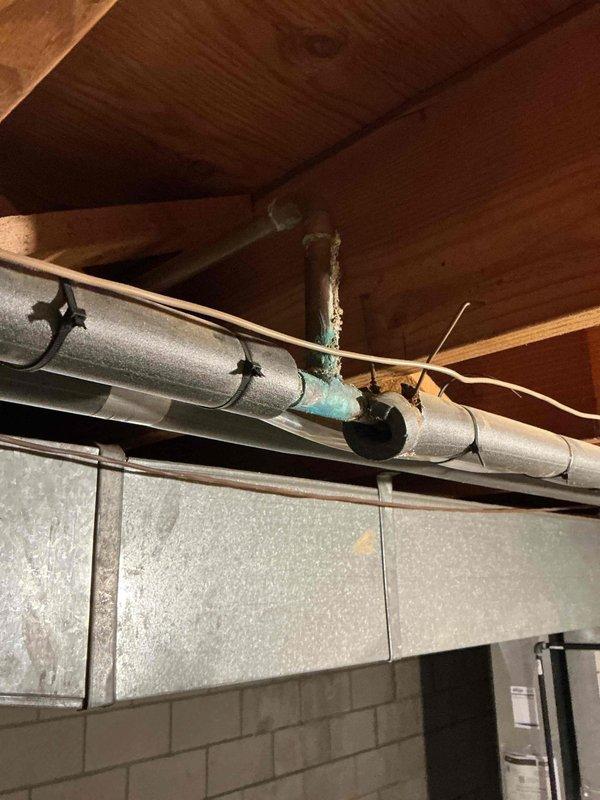 Responded to service call for slow kitchen drain with suspected damage in floor. Upon inspection of basement utility area beneath kitchen, discovered severely corroded copper pipe connection with extensive green oxidation and mineral deposits indicating long-term water damage and moisture exposure. The deteriorated pipe joint showed significant verdigris buildup and compromised integrity, which was contributing to drainage issues above. Documented existing conditions including corroded copper piping, HVAC ductwork proximity, and basement infrastructure for repair recommendations.