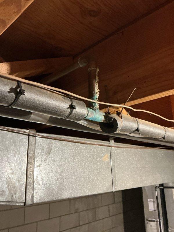 Responded to service call for slow kitchen drain with suspected damage in floor. Upon inspection of basement utility area beneath kitchen, discovered severely corroded copper pipe connection with extensive green oxidation and mineral deposits indicating long-term water damage and moisture exposure. The deteriorated pipe joint showed significant verdigris buildup and compromised integrity, which was contributing to drainage issues above. Documented existing conditions including corroded copper piping, HVAC ductwork proximity, and basement infrastructure for repair recommendations.
