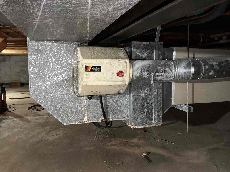 Conducted comprehensive site assessment for complete HVAC system replacement in residential basement installation. Evaluated existing Armstrong furnace/air handler unit and associated ductwork infrastructure, including galvanized metal duct transitions and reflective insulation materials. Documented current system configuration, noting equipment positioning beneath floor joists, PVC condensate drainage lines, electrical conduit routing, and existing duct mounting hardware. Photographed installation area to support replacement estimate specifications, capturing equipment clearances, structural considerations, and accessibility factors for future system removal and new equipment installation.