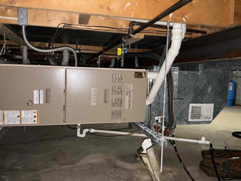 Conducted comprehensive site assessment for complete HVAC system replacement in residential basement installation. Evaluated existing Armstrong furnace/air handler unit and associated ductwork infrastructure, including galvanized metal duct transitions and reflective insulation materials. Documented current system configuration, noting equipment positioning beneath floor joists, PVC condensate drainage lines, electrical conduit routing, and existing duct mounting hardware. Photographed installation area to support replacement estimate specifications, capturing equipment clearances, structural considerations, and accessibility factors for future system removal and new equipment installation.