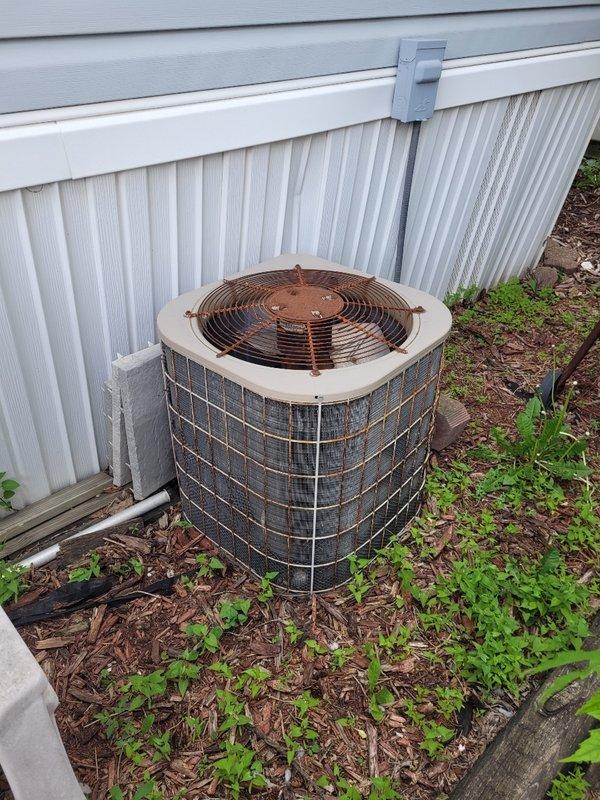 Responded to no cooling call on residential air conditioning system over 10 years old. Upon arrival, found outdoor condenser unit showing significant age-related wear with darkened grille components and vegetation growth restricting airflow around the base. Unit requires preventive maintenance appointment to address accumulated debris, verify refrigerant charge, and assess overall system performance to restore proper cooling operation.