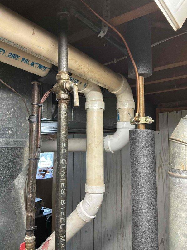 Conducted on-site assessment of 14-year-old residential water heater showing visible corrosion and rust deterioration on bottom tank surface. Documented existing plumbing configuration including PVC drainage system, copper supply lines with insulation, and brass shut-off valve connections. Provided comprehensive replacement estimate for new water heater installation to address structural integrity concerns before potential tank failure occurs.