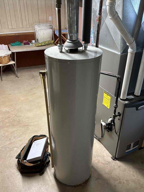Conducted on-site assessment of 14-year-old residential water heater showing visible corrosion and rust deterioration on bottom tank surface. Documented existing plumbing configuration including PVC drainage system, copper supply lines with insulation, and brass shut-off valve connections. Provided comprehensive replacement estimate for new water heater installation to address structural integrity concerns before potential tank failure occurs.