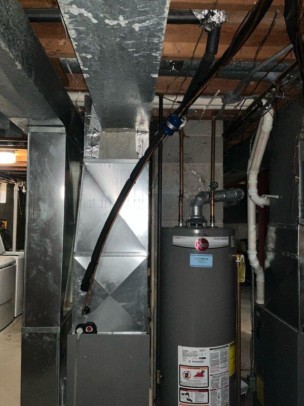 Conducted on-site evaluation of existing HVAC air handler system located in basement utility space and provided replacement estimate. Documented current equipment configuration including vertical air handler unit with 16x20x1 filter specifications, associated metallic ductwork showing dust accumulation and surface staining, and overall mechanical room layout with water heater and existing utility infrastructure. Assessed installation environment including concrete floor conditions, exposed ceiling joists, and existing duct routing to determine replacement specifications and system requirements.