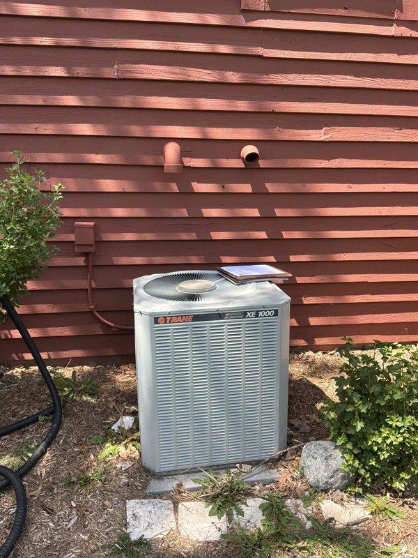 Conducted comprehensive site assessment for complete air conditioning system replacement at residential property with forced air furnace system in basement. Evaluated existing Trane XE 1000 outdoor condensing unit positioned on concrete pad against perimeter fence, noting unit failure and need for full system replacement. Assessed refrigerant line routing, electrical service panel capacity and circuit breaker configuration, and existing infrastructure to determine equipment specifications and installation requirements for new HVAC system replacement.