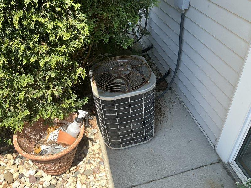 Completed comprehensive HVAC system evaluation for air conditioning replacement estimate at residential property. Assessed existing outdoor cylindrical condenser unit showing weather-related wear and indoor furnace/air handler equipment located in utility area alongside water heater. Documented current system configuration including electrical connections, refrigerant line routing, condensate drainage, and equipment placement on exterior concrete pad with landscaping considerations. Photographed both indoor and outdoor components to provide detailed equipment specifications and installation parameters for replacement system proposal.