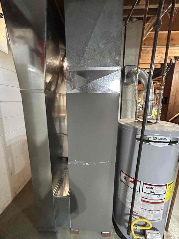 Completed installation of new air conditioning system with evaporator coil in residential basement utility area. System includes new air handler unit positioned vertically with proper clearances for maintenance access, connected to existing ductwork via flexible aluminum ducting with appropriate elbow configurations. All refrigerant lines, electrical connections, and condensate drainage installed to manufacturer specifications and local code requirements.
