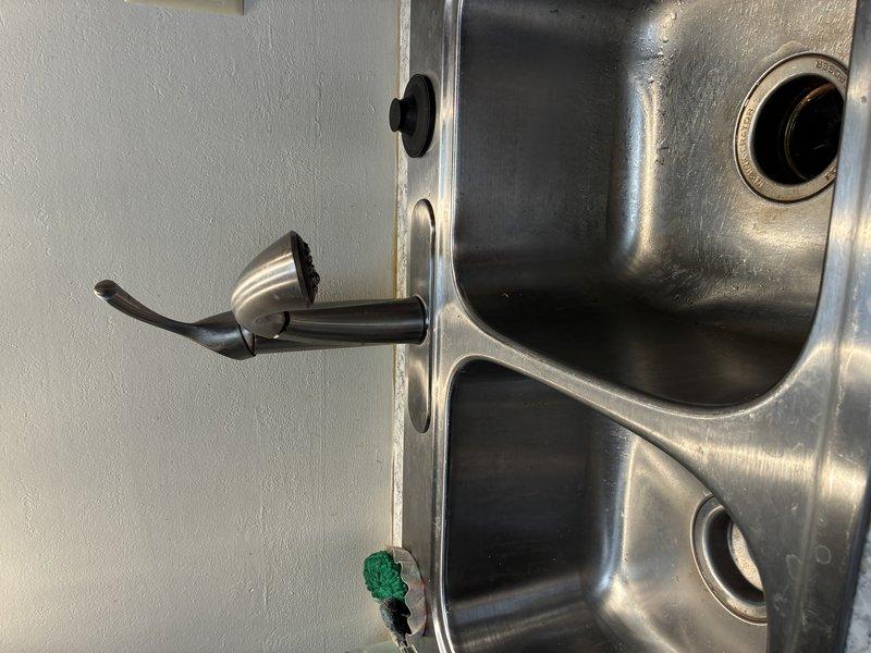 Installed customer-supplied single-handle kitchen faucet on double-basin stainless steel sink. Completed mounting and connection of the modern tall-spout faucet with black accent handle, ensuring proper positioning between basins and verifying all supply line connections for leak-free operation.