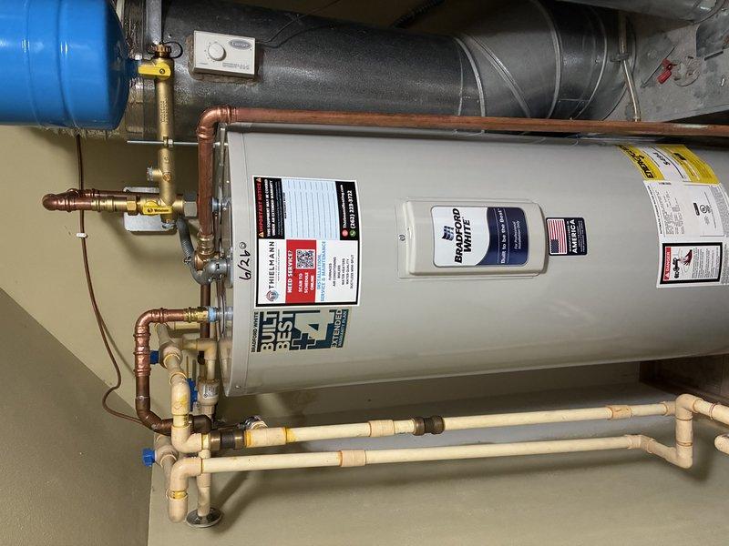 Completed installation of Bradford White tanked water heater in residential utility room. Connected all supply and distribution lines using copper piping with brass fittings and shut-off valves, integrated existing PVC/CPVC manifold system at floor level, and installed blue expansion tank with proper copper connections. Verified all connections for leaks, ensured proper venting, and confirmed system operation upon completion.