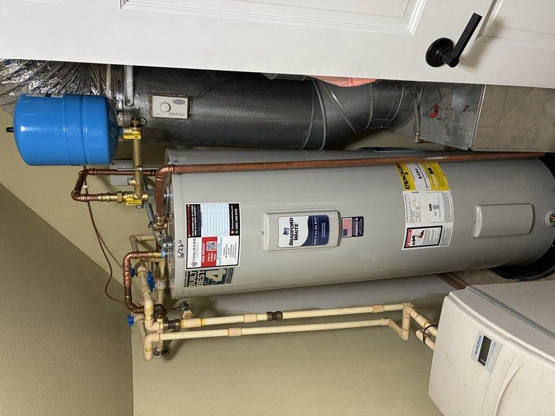 Completed installation of Bradford White tanked water heater in residential utility room. Connected all supply and distribution lines using copper piping with brass fittings and shut-off valves, integrated existing PVC/CPVC manifold system at floor level, and installed blue expansion tank with proper copper connections. Verified all connections for leaks, ensured proper venting, and confirmed system operation upon completion.