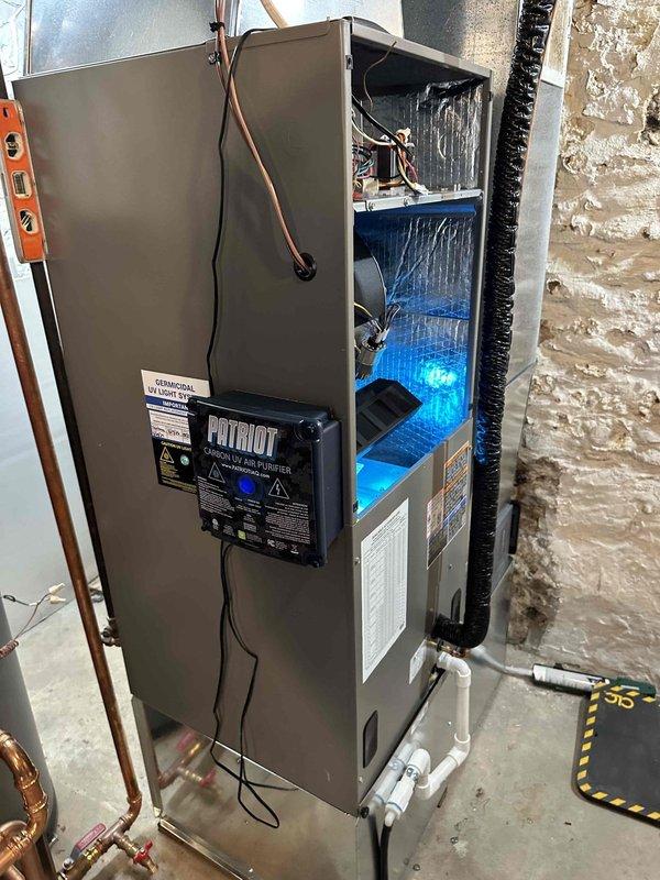 Completed installation of new air handler unit in basement location. Installed Patriot control module, connected refrigerant lines, configured electrical wiring and controls with multi-colored low-voltage connections, and integrated supply and return ductwork with flexible silver ducting. Unit tested and operational with evaporator coil assembly properly illuminated and functioning.
