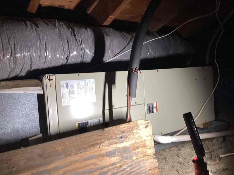 Responded to no cooling complaint with attic unit freezing over. Upon inspection, found residential split system HVAC equipment located in attic space with outdoor condensing unit mounted on exterior platform. Documented equipment information including manufacturer data from unit labels for aging system over 10 years old. Assessed frozen evaporator coil condition and identified potential causes including restricted airflow, low refrigerant charge, or failed blower motor operation. Verified ductwork connections and insulation integrity in attic installation. Inspected outdoor unit for proper operation, checked refrigerant line insulation running along exterior wall, and evaluated condensate drainage system. Provided customer with equipment age assessment, diagnostic findings, and repair recommendations to restore cooling function and prevent future freeze-up conditions.