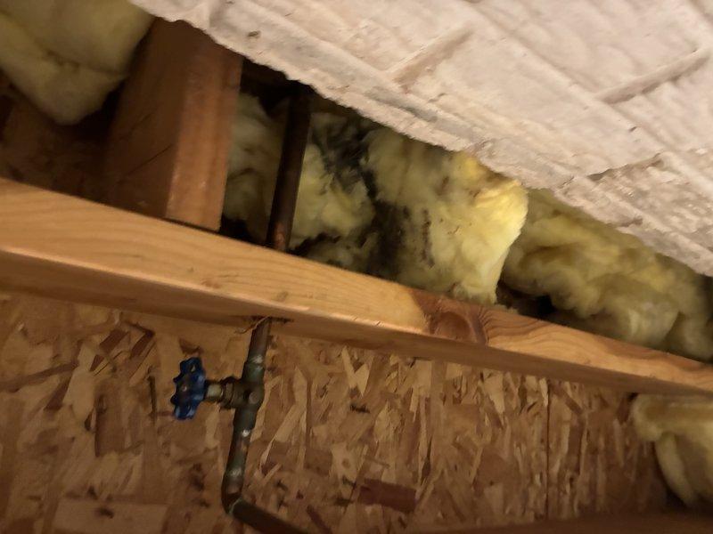 Responded to service call for leaking hose bib. Upon arrival, performed diagnostic inspection and traced water supply line through attic space to locate source of leak. Identified defective outdoor spigot fixture causing water intrusion. Accessed copper supply piping running through upper floor framing and insulation to assess connection points and verify extent of leak. Documented existing conditions including plumbing infrastructure, structural framing, and insulation placement for repair recommendations.