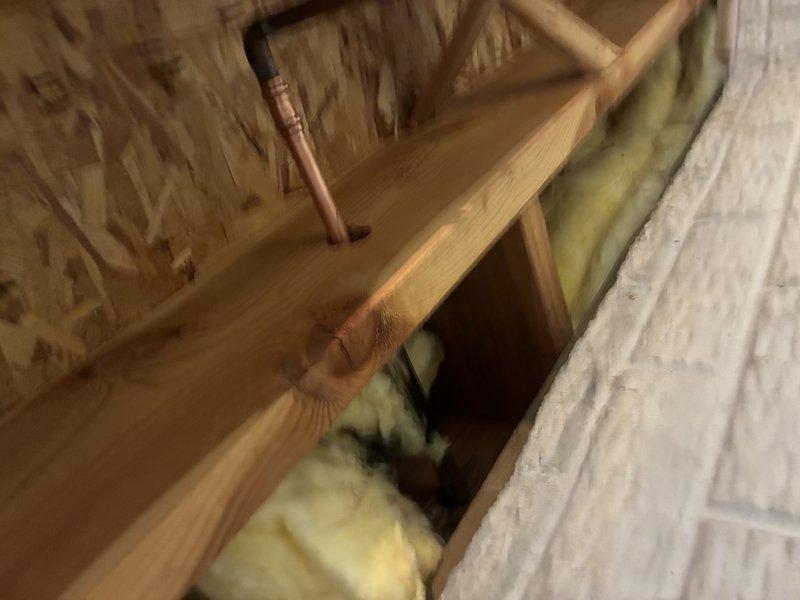 Responded to service call for leaking hose bib. Upon arrival, performed diagnostic inspection and traced water supply line through attic space to locate source of leak. Identified defective outdoor spigot fixture causing water intrusion. Accessed copper supply piping running through upper floor framing and insulation to assess connection points and verify extent of leak. Documented existing conditions including plumbing infrastructure, structural framing, and insulation placement for repair recommendations.