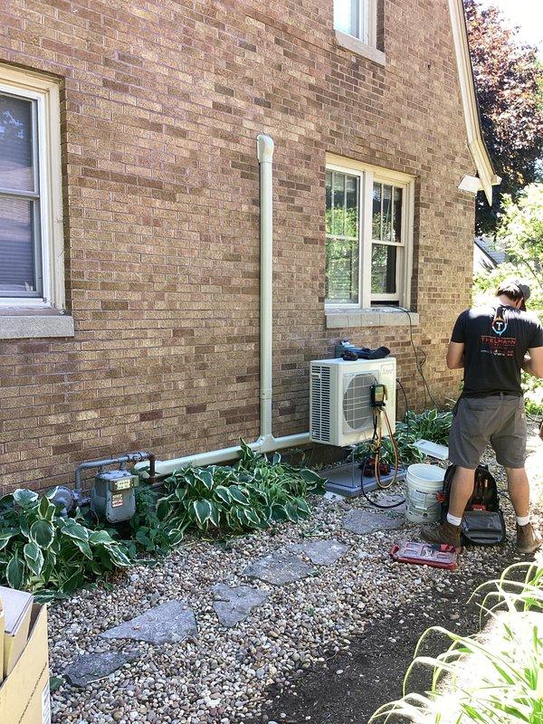 # HVAC Mini Split Installation

Completed full installation of ductless mini split air conditioning system for residential property. Mounted outdoor condenser unit on concrete pad at exterior foundation with proper clearances and secure mounting. Ran refrigerant lines, electrical connections, and condensate drain through exterior wall penetration with appropriate sealing. Installed indoor air handler unit on interior wall at optimal height for air distribution. System positioned in living space with two-tone painted walls, mounted above existing radiator heating system. Completed all electrical connections from outdoor unit to indoor evaporator, secured line set with proper insulation and protection. Tested system operation, verified refrigerant charge, confirmed proper drainage, and ensured all connections were leak-free and secure. System commissioned and left in full working order.