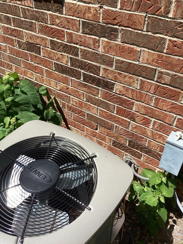 Completed full HVAC system installation including new furnace and air conditioning unit at residential property. Installed outdoor condensing unit against exterior brick wall with proper clearances and mounted on level pad. Unit features top-discharge fan configuration with protective grill. Ran refrigerant lines and electrical connections from outdoor unit through exterior wall penetration. Connected condensate drain line using PVC piping with proper pitch for drainage. Verified all connections are secure and sealed. System positioned to allow adequate airflow and future service access. Installation includes both heating and cooling components as complete comfort system replacement. All work performed to manufacturer specifications and local code requirements.
