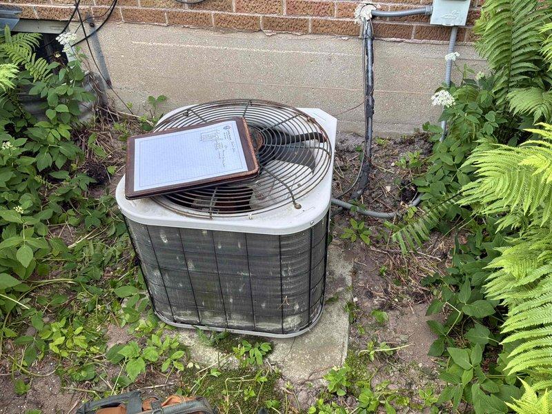 Conducted on-site evaluation of existing air conditioning system for proactive replacement estimate. The current outdoor condensing unit, which has been in service for over 20 years, remains operational but has reached the end of its expected service life. Documented existing equipment installation including electrical panel configuration and outdoor unit placement on concrete pad adjacent to brick exterior wall. Photographed circuit breaker panel showing current electrical service and outdoor condenser unit positioned in landscaped area with proper clearances. Provided comprehensive replacement options and recommendations for new high-efficiency cooling system to ensure continued reliable operation and improved energy performance.