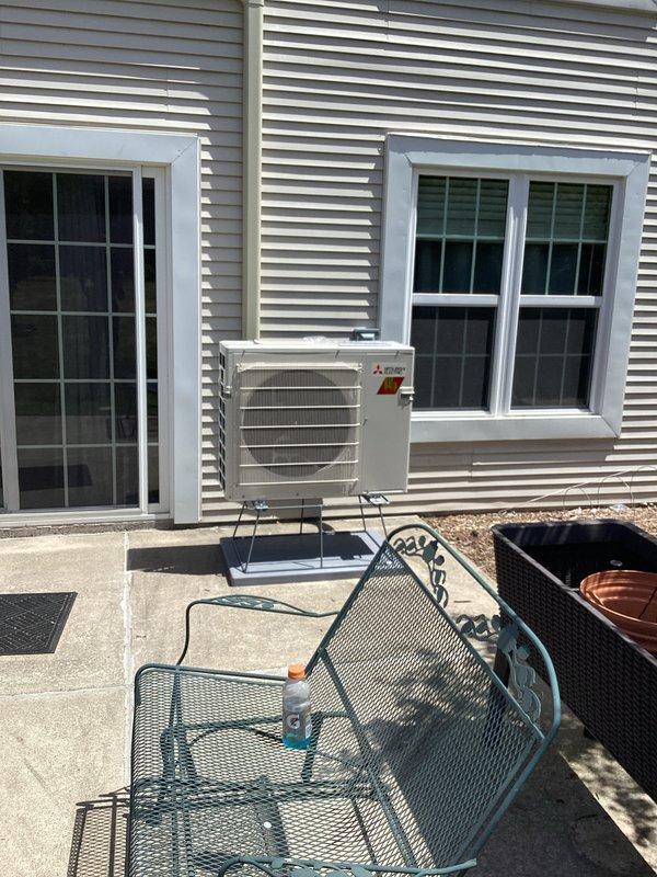 Completed installation of Mitsubishi ductless mini-split heat pump system. Mounted outdoor condenser unit on exterior wall bracket between two windows on beige vinyl siding. Installed indoor air handler on interior wall near ceiling in residential room with proper clearances maintained. Ran refrigerant lines and electrical connections between indoor and outdoor units. System tested and confirmed operational upon completion.