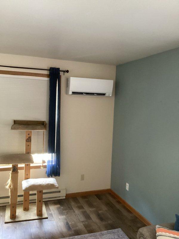 Completed installation of Mitsubishi ductless mini-split heat pump system. Mounted outdoor condenser unit on exterior wall bracket between two windows on beige vinyl siding. Installed indoor air handler on interior wall near ceiling in residential room with proper clearances maintained. Ran refrigerant lines and electrical connections between indoor and outdoor units. System tested and confirmed operational upon completion.