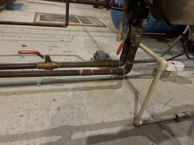 Responded to service call for non-recycling water softener experiencing calcium buildup and clogging issues. Performed diagnostic inspection of water treatment system and associated plumbing infrastructure including copper supply lines, PVC discharge piping, and control valve assembly. Evaluated system operability and documented current condition of equipment with photographic evidence showing piping configuration, mounting hardware, and overall installation setup in utility area.