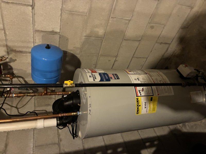 Completed installation of Bradford White tanked water heater in basement utility area. Installed new unit with proper plumbing connections including copper piping with soldered joints, brass fittings, and shut-off valve. Mounted blue expansion tank on wall and connected to system per manufacturer specifications. Verified all connections, tested system operation, and ensured compliance with plumbing codes and safety requirements.