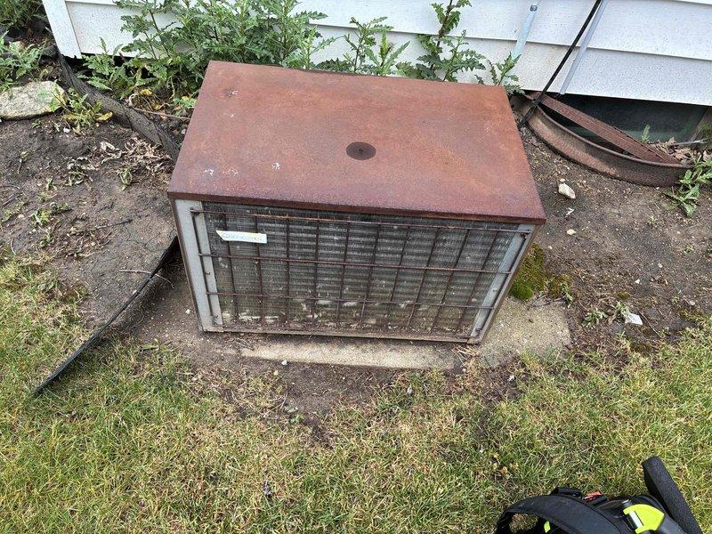 Responded to no cooling call on aging outdoor condensing unit that failed over the weekend with abnormal noise reported. Upon arrival, found heavily weathered unit with significant rust deterioration on top panel and overgrown vegetation restricting airflow around cabinet. Performed diagnostic evaluation to determine cause of cooling failure and unusual operational sounds. Documented unit condition showing extensive exterior corrosion and lack of maintenance clearance around equipment. Customer notified of findings for repair options on system exceeding 10-year service life.