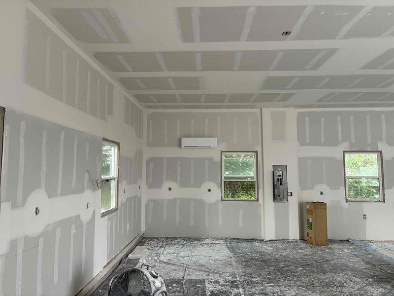Completed installation of mini-split air conditioning system in residential space undergoing renovation. Mounted indoor wall unit in main room between windows with proper electrical connections, installed outdoor condenser unit on concrete pad with decorative gravel base, and performed system commissioning with digital gauges to verify proper refrigerant pressures and operation.