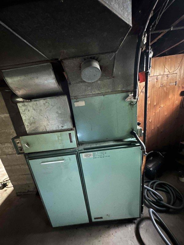Conducted on-site HVAC system evaluation for equipment replacement estimate. Assessed existing older model furnace and air conditioning system with distinctive turquoise-colored cabinet configuration installed in basement utility area. Documented current equipment condition, ductwork configuration, electrical connections, and spatial constraints through photographic documentation to support replacement proposal and system sizing requirements.