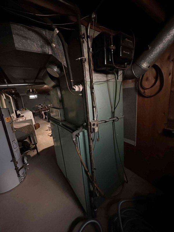 Conducted on-site HVAC system evaluation for equipment replacement estimate. Assessed existing older model furnace and air conditioning system with distinctive turquoise-colored cabinet configuration installed in basement utility area. Documented current equipment condition, ductwork configuration, electrical connections, and spatial constraints through photographic documentation to support replacement proposal and system sizing requirements.