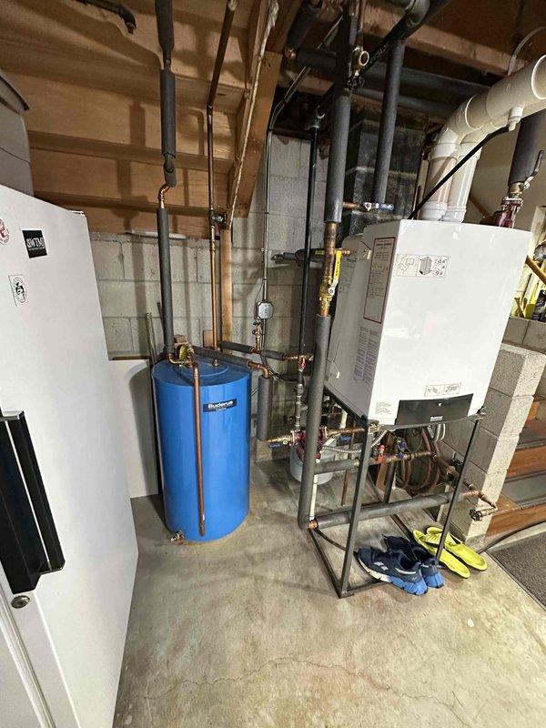 Completed on-site estimate for boiler and indirect water heater replacement. Existing heating system showing signs of failure, requiring full replacement of boiler unit and indirect tank. Documented current equipment configuration including wall-mounted boiler, cylindrical indirect water storage tank, associated copper piping with brass fittings, gas lines, and PVC venting system. Photographed exterior venting termination points and interior mechanical room layout to provide comprehensive assessment for equipment replacement proposal.