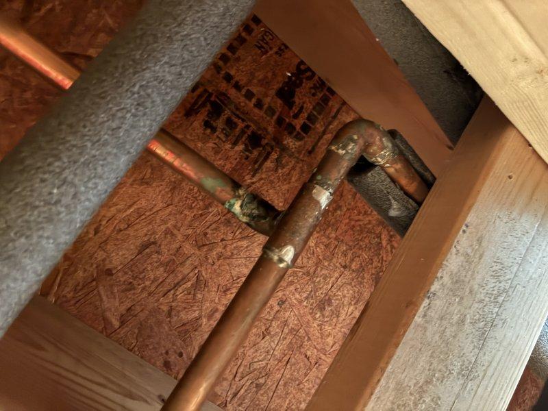 Completed diagnostic inspection of leaking copper plumbing in basement floor cavity. Upon inspection, identified corroded copper pipe sections with visible green patina at joints and connection points, requiring full replacement. Documented existing conditions including aged copper piping, deteriorating fittings, and compromised pipe integrity through access opening in floor joists.