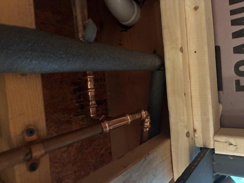 Completed diagnostic inspection of leaking copper plumbing in basement floor cavity. Upon inspection, identified corroded copper pipe sections with visible green patina at joints and connection points, requiring full replacement. Documented existing conditions including aged copper piping, deteriorating fittings, and compromised pipe integrity through access opening in floor joists.