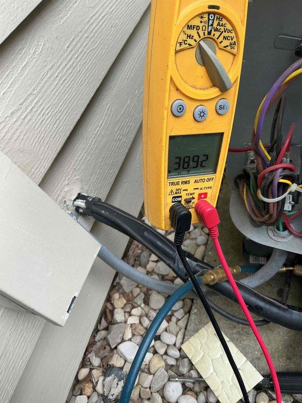 # HVAC Service Call - No Cooling Complaint

Responded to a no cooling complaint on a residential air conditioning system. Upon arrival, located the outdoor condensing unit installed on a gravel pad against the home's exterior. Performed initial visual inspection of the condenser unit, noting the system's age and overall condition.

Conducted electrical diagnostics using a digital multimeter to test voltage and electrical connections at the outdoor unit. Measured line voltage at the condenser, obtaining a reading of approximately 39 volts, which is significantly below the required 208-240 volt range for proper compressor and condenser fan motor operation. This low voltage condition would prevent the unit from starting and operating correctly.

Traced electrical wiring including the purple, brown, and red conductors running to the unit. Inspected the electrical disconnect, contactor, and capacitor connections. The substantially reduced voltage indicated either an upstream electrical supp