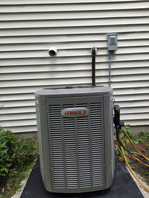 Completed full HVAC system installation including new furnace and air conditioning unit with all required permits and electrical work. Installed brown metal furnace unit in basement mechanical room with properly configured silver ductwork connecting to overhead distribution system, including both rectangular and cylindrical metal sections running along ceiling joists. Mounted new Lennox brand condenser unit on black rubber pad against exterior wall with proper refrigerant line routing and electrical disconnect, ensuring all connections meet code requirements and manufacturer specifications.