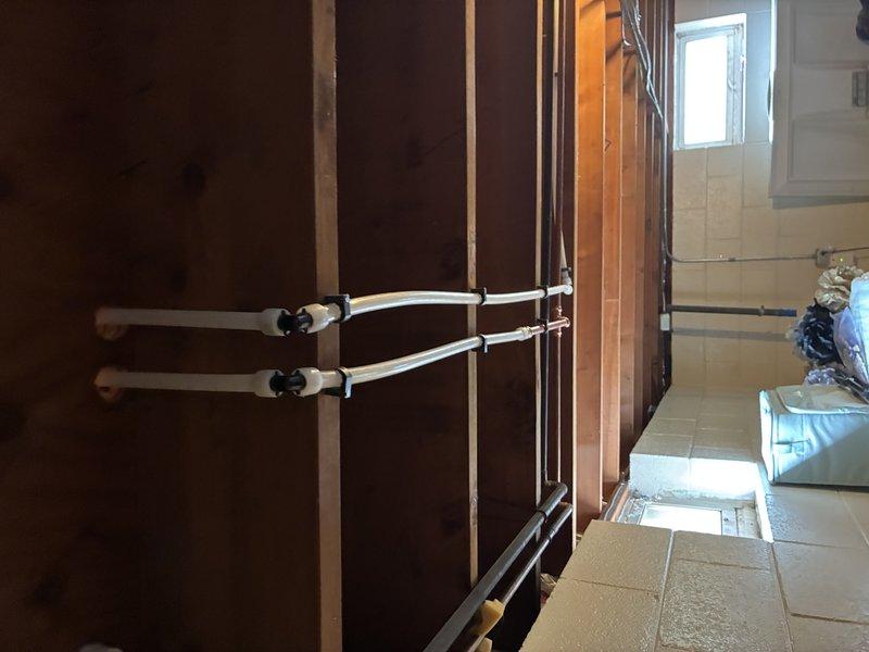 Completed laundry relocation installation with new water supply lines and drain piping. Installed hot and cold water valve assemblies with brass fittings and control handles mounted on wall bracket within framed cavity, routed PVC supply and drain lines through wall structure with proper support and securing hardware, and positioned all plumbing components to accommodate relocated laundry equipment per specifications.