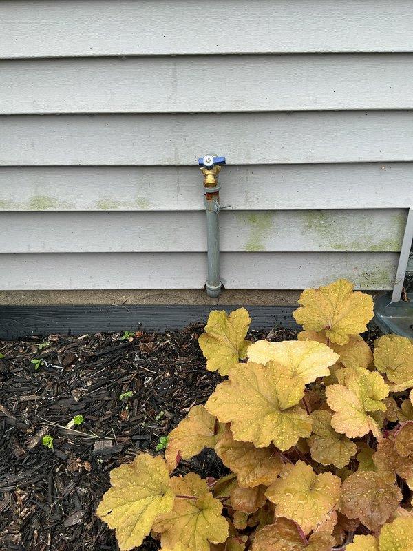 Responded to leaking outdoor water spigot. Inspected exterior hose bib with blue handle and brass fittings mounted on gray PVC riser pipe along building exterior. Traced supply line to interior shutoff valve in basement utility area where copper and PVC plumbing runs were accessible along ceiling joists. Replaced faulty valve components and verified all connections were secure with no active leaks upon testing water flow.