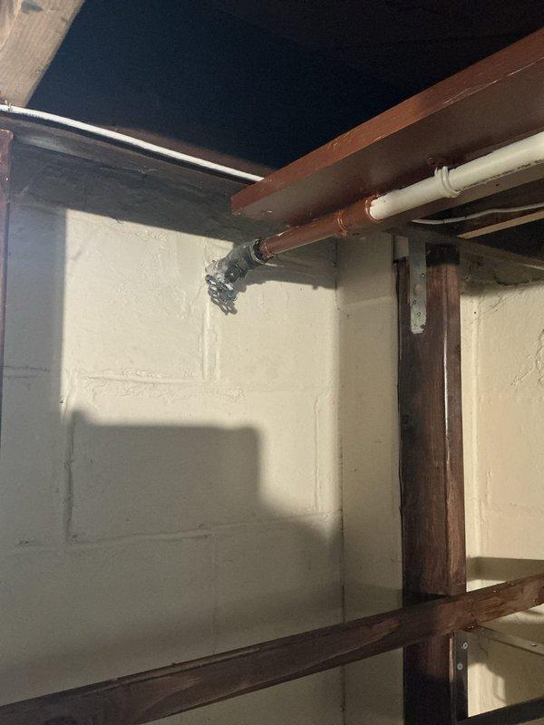 Responded to leaking outdoor water spigot. Inspected exterior hose bib with blue handle and brass fittings mounted on gray PVC riser pipe along building exterior. Traced supply line to interior shutoff valve in basement utility area where copper and PVC plumbing runs were accessible along ceiling joists. Replaced faulty valve components and verified all connections were secure with no active leaks upon testing water flow.