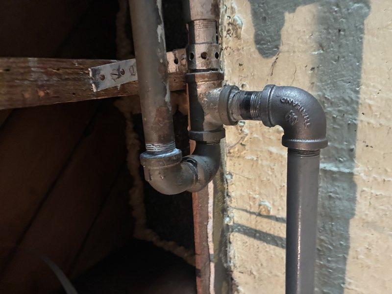 Responded to gas leak service call following utility company inspection that identified three leaks requiring repair. Performed diagnostic assessment of gas piping system in basement utility area, examining exposed gas lines, fittings, and connections. Inspected cast iron elbow joints, copper piping, and associated gas line components showing age-related deterioration and corrosion. Documented conditions of threaded connections, horizontal pipe runs, and vertical risers where leaks were detected. Photographed affected areas including deteriorated fittings at wall penetrations and corroded pipe sections with visible rust. Confirmed locations of reported leaks and assessed overall system integrity to determine necessary repairs.