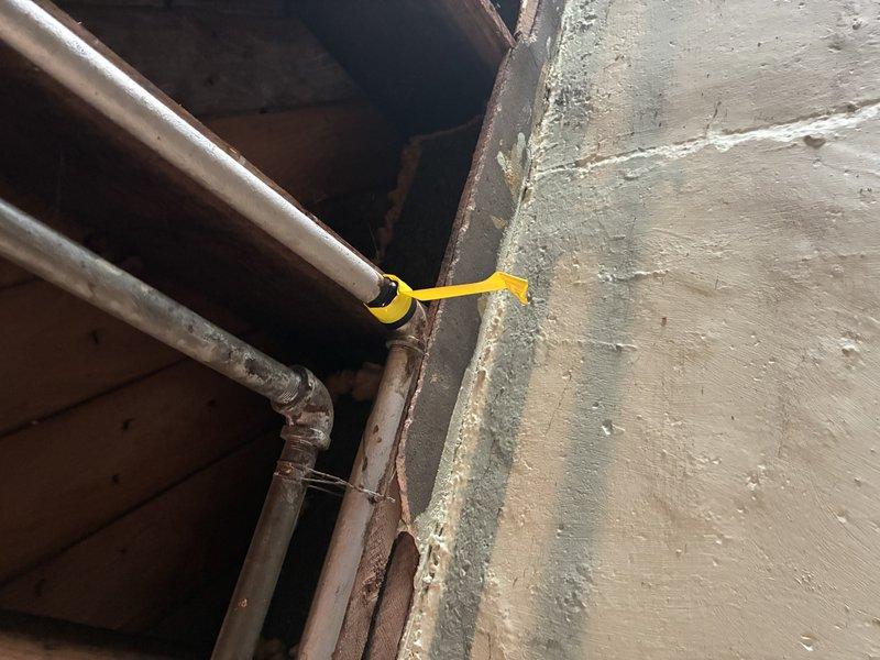 Responded to gas leak service call following utility company inspection that identified three leaks requiring repair. Performed diagnostic assessment of gas piping system in basement utility area, examining exposed gas lines, fittings, and connections. Inspected cast iron elbow joints, copper piping, and associated gas line components showing age-related deterioration and corrosion. Documented conditions of threaded connections, horizontal pipe runs, and vertical risers where leaks were detected. Photographed affected areas including deteriorated fittings at wall penetrations and corroded pipe sections with visible rust. Confirmed locations of reported leaks and assessed overall system integrity to determine necessary repairs.