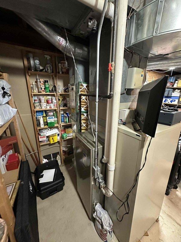 Conducted furnace replacement estimate in residential basement utility area. Evaluated existing beige furnace unit with overhead silver ductwork and white PVC condensate piping, documenting current system configuration and mechanical room layout for complete HVAC system replacement proposal.