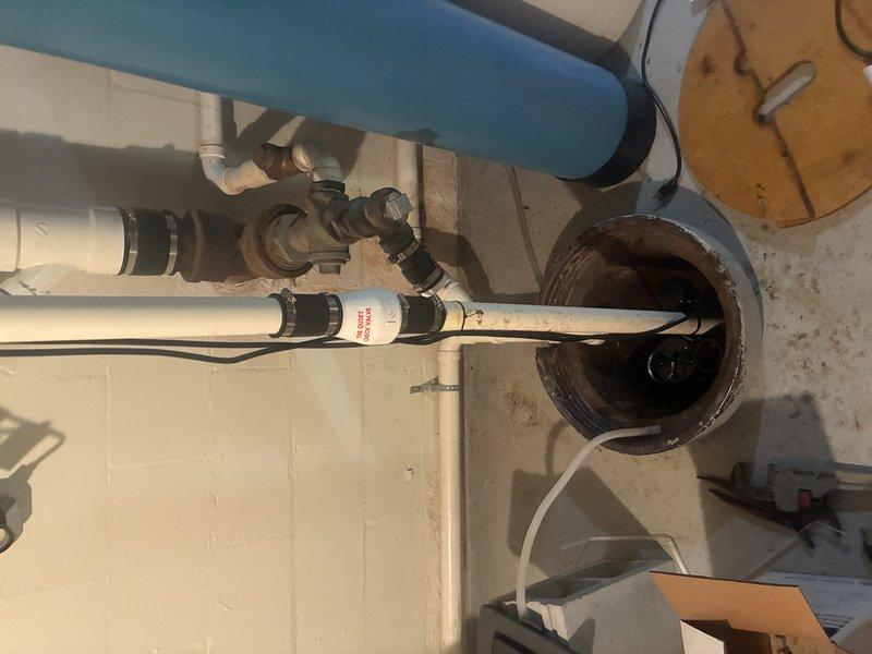 Completed installation of new sump pump system in basement utility area. Installed pump unit in existing sump pit with proper discharge piping configuration, including white PVC discharge lines with multiple connection points, valves, and fittings for optimal water removal. Connected system to blue pressure tank with integrated pressure switch and wiring to ensure automatic operation and proper cycling.