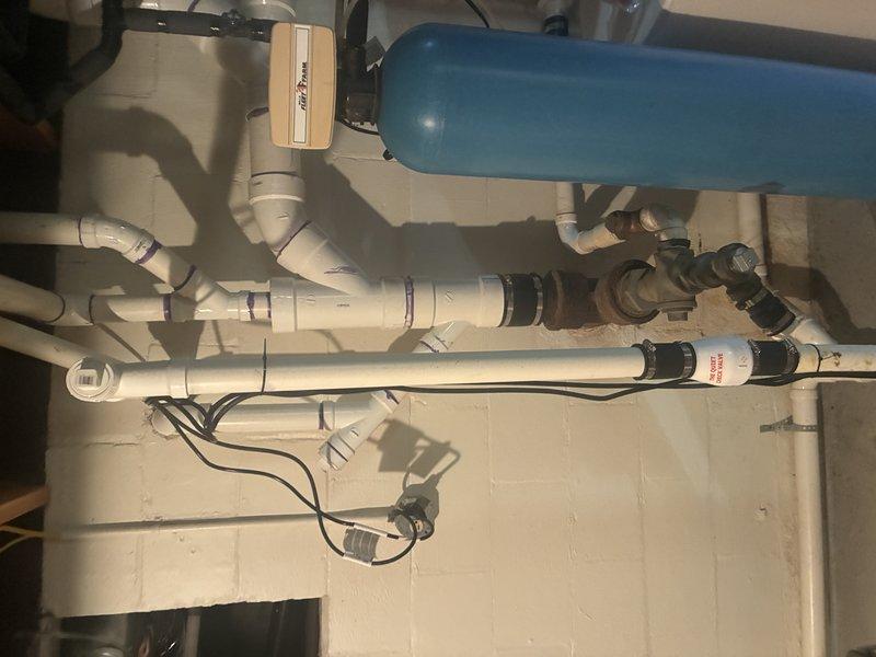 Completed installation of new sump pump system in basement utility area. Installed pump unit in existing sump pit with proper discharge piping configuration, including white PVC discharge lines with multiple connection points, valves, and fittings for optimal water removal. Connected system to blue pressure tank with integrated pressure switch and wiring to ensure automatic operation and proper cycling.
