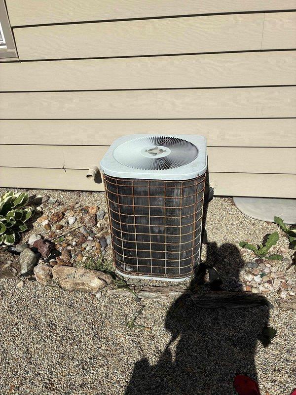 Conducted on-site estimate for complete HVAC system replacement including gas furnace currently located in basement and outdoor air conditioning condenser unit. Evaluated existing equipment condition, documented current installation with photographs showing AC unit positioned on concrete pad with gravel landscaping against building exterior, and provided homeowner with replacement options and specifications for both heating and cooling systems.
