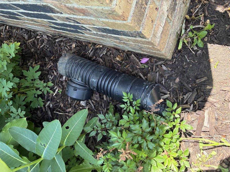 Responded to a diagnostic service call for a malfunctioning sump pump discharge system. Upon inspection, identified two critical issues: a leak at the exterior connector where the discharge hose attaches to the sump pump, and a disconnected discharge pipe at the underground culvert connection point. Documented the faulty connections and deteriorated hose clamps with photographic evidence showing the corrugated flexible drainage components, PVC fittings, and compromised connection points at the building foundation. The disconnected underground pipe junction was preventing proper water evacuation from the sump system, creating potential flooding risk and foundation damage concerns.