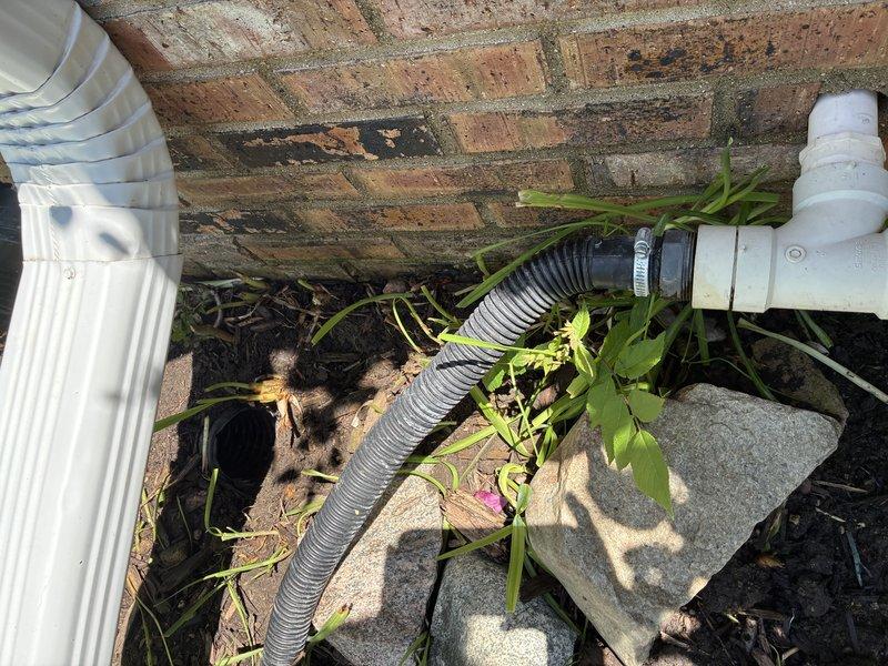 Responded to a diagnostic service call for a malfunctioning sump pump discharge system. Upon inspection, identified two critical issues: a leak at the exterior connector where the discharge hose attaches to the sump pump, and a disconnected discharge pipe at the underground culvert connection point. Documented the faulty connections and deteriorated hose clamps with photographic evidence showing the corrugated flexible drainage components, PVC fittings, and compromised connection points at the building foundation. The disconnected underground pipe junction was preventing proper water evacuation from the sump system, creating potential flooding risk and foundation damage concerns.