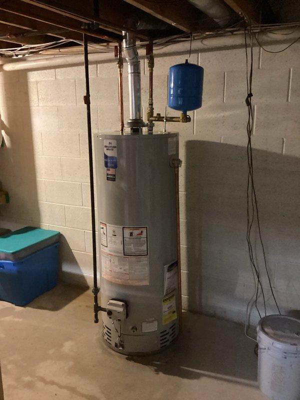 Completed residential water heater installation in basement utility area. Retrieved new unit from Ferguson supply house and coordinated arrival with customer onsite. Installed tall cylindrical water heater with proper connections to existing plumbing system, including copper supply lines and flexible connectors. Mounted blue expansion tank horizontally above unit and connected to water system. Installed metallic flue piping for proper venting. Verified all connections to electrical panel and ensured proper grounding and circuit protection. Tested system operation and confirmed no leaks at all connection points.
