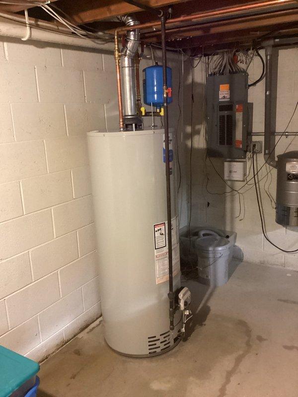 Completed residential water heater installation in basement utility area. Retrieved new unit from Ferguson supply house and coordinated arrival with customer onsite. Installed tall cylindrical water heater with proper connections to existing plumbing system, including copper supply lines and flexible connectors. Mounted blue expansion tank horizontally above unit and connected to water system. Installed metallic flue piping for proper venting. Verified all connections to electrical panel and ensured proper grounding and circuit protection. Tested system operation and confirmed no leaks at all connection points.