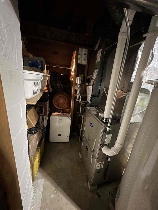 Completed on-site assessment for HVAC system replacement in residential basement utility area. Evaluated existing Carrier furnace/air handler unit, associated ductwork, and available installation space. Documented current equipment configuration, clearances, and mechanical room conditions including water heater proximity, storage constraints, and existing PVC venting arrangement. Photographed equipment access points and utility connections to develop comprehensive replacement estimate.