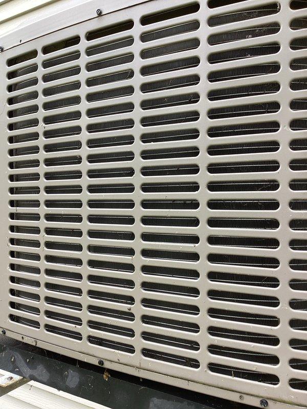 Responded to no cooling complaint on aging residential air conditioning system. Upon arrival, found ice buildup on exterior refrigerant lines and unit not producing cold air. Documented outdoor condensing unit condition showing weathered components, oxidized copper refrigerant lines, and aged equipment connections consistent with 10+ year old system. Unit was already turned off by customer prior to arrival due to freezing condition. Inspected exterior grille, refrigerant line connections, and overall equipment condition to assess system status and determine appropriate next steps for restoring cooling operation.